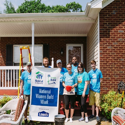 Women and men on front porch of house holding a banner