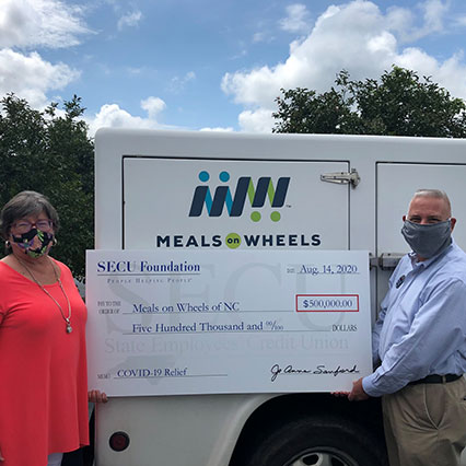 Man and woman holding big check in front of Meals on Wheels truck
