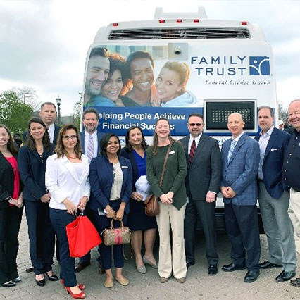 Large group of men and women standing in front of bus with Family Trust FCU logo behind them